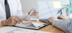 A professional image of two business professionals analyzing graphs and charts on a clipboard and laptop. The setting is a bright office, symbolizing data-driven solutions and ISO certification services.